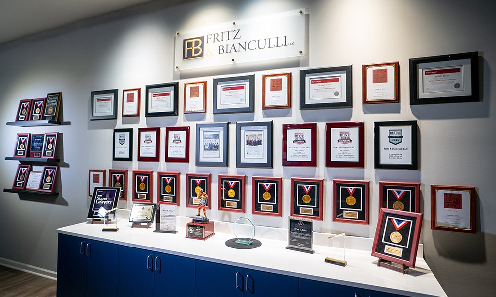 Wall of framed awards and recognitions at the Fritz & Bianculli law office